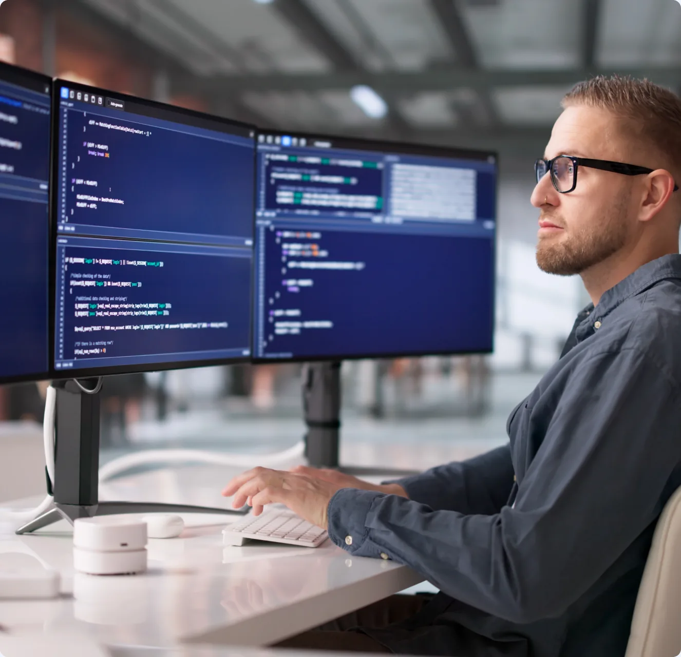 A developer at a desk working across two monitors of code in a bright office